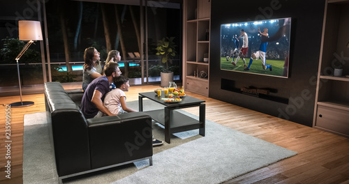 A family is watching a soccer moment on the TV and celebrating a goal, sitting on the couch in the living room. photo