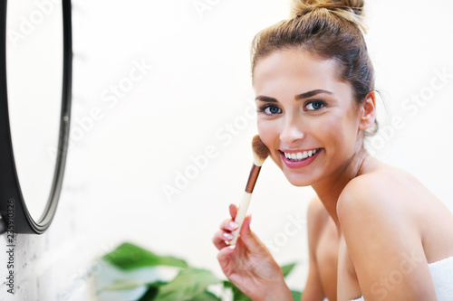 Young woman applying makeup with brush in bathroom