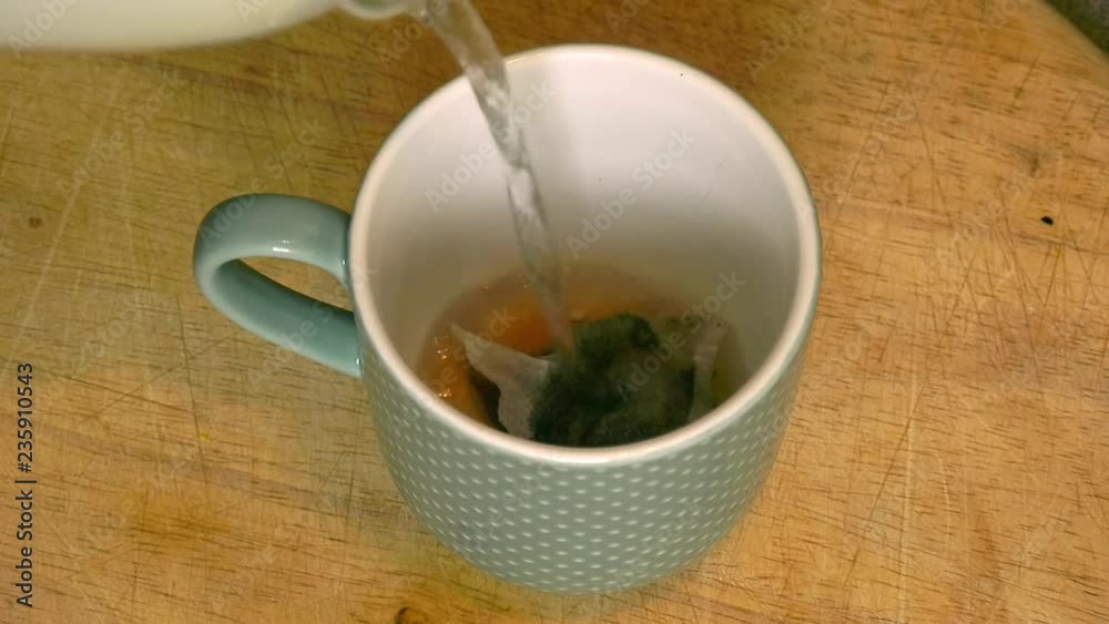 Boiling water is poured into a cup containing a tea bag Boiling water is poured into a cup containing a tea bag