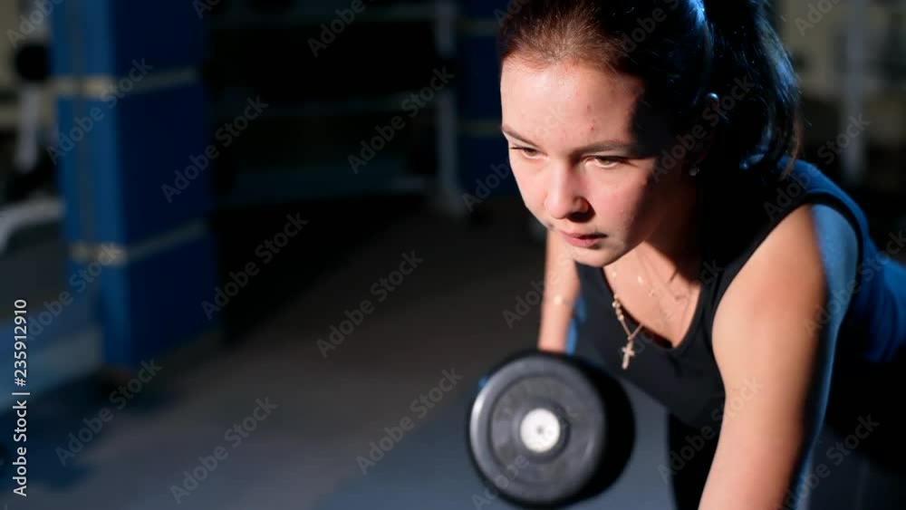 A girl performs a dumbbell with one hand in the slope using a bench. exercise on the broadest back muscles with dumbbells. A girl performs a dumbbell with one hand in the slope using a bench. exercise on the broadest back muscles with dumbbells.
