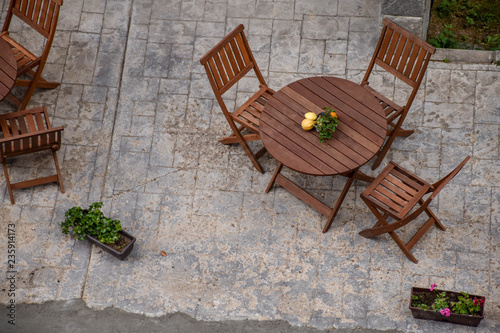 Top view of a wooden restaurant table with chairs, adorned with fruit, in front of a hotel