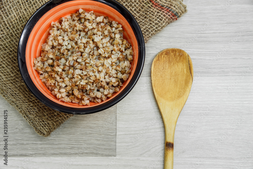 Buckwheat porridge in a plate on a light gray wooden background. View from above.