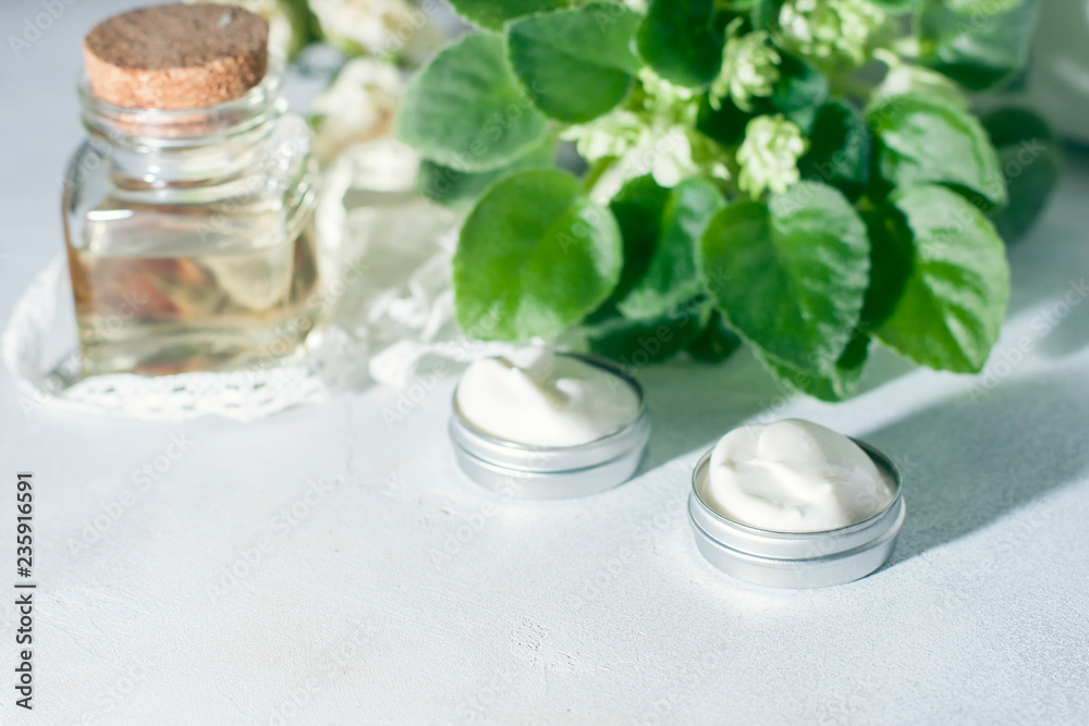 cosmetic cream with flowers on a light stone background.