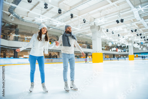 happy couple holding hands while skating on rink together