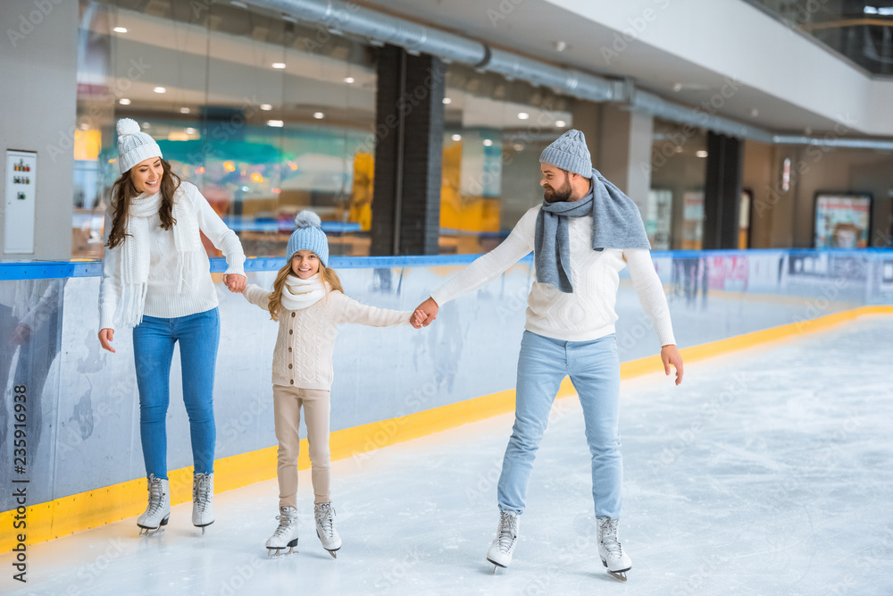 cheerful family in sweaters holding hands while skating together on ice rink