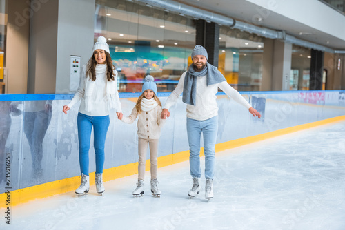 happy family holding hands while skating together on ice rink