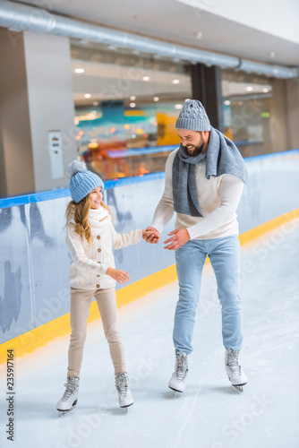 father and daughter in knitted sweaters skating on ice rink together