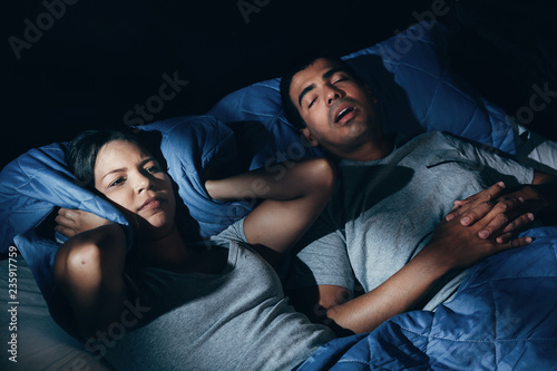 Fotografie Annoyed woman lying in bed with snoring boyfriend at home in the bedroom