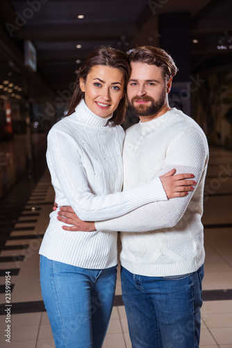 smiling couple in white sweaters hugging and looking at camera
