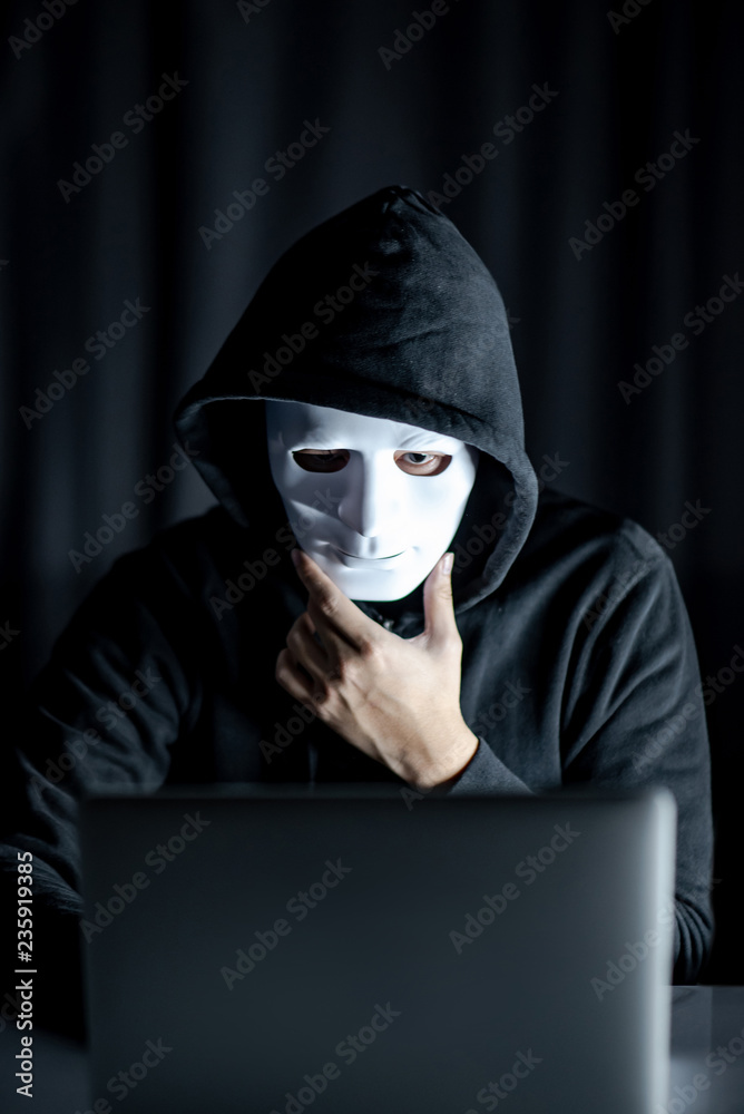 Mystery male hoodie hacker holding white mask looking at laptop computer.  Anonymous social masking. Ransomware cyber attack or internet security  concepts Stock Photo | Adobe Stock