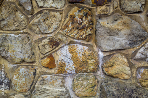 A close-up of an ornate sandstone wall made up of random shapes and sizes of stones. Rustic textured background or flat lay concept.