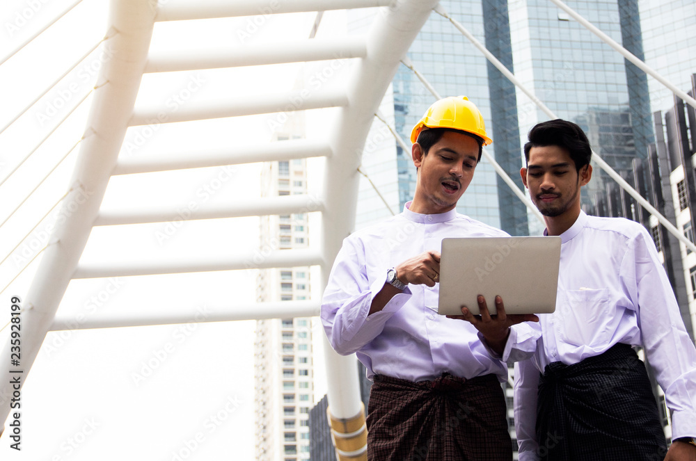 Two young engineers holding smart phone device and offices building background. Two young engineers holding smart phone device and offices building background.