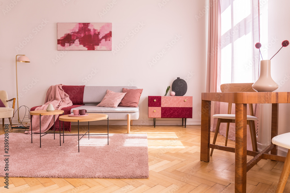 Flowers on wooden table in pink apartment interior with sofa under poster next to cabinet. Real photo - obrazy, fototapety, plakaty 