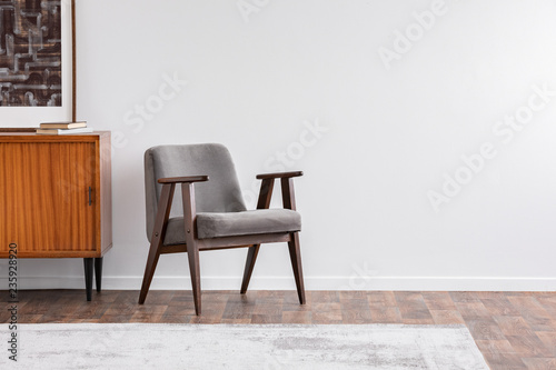 Grey vintage armchair next to retro cabinet with books, warm carpet on wooden fool, real photo
