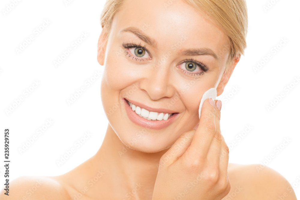 Studio close up of a gorgeous happy woman with healthy perfect skin cleansing her face with a cotton pad smiling to the camera isolated on white beauty cosmetology spa skincare freshness youth smooth