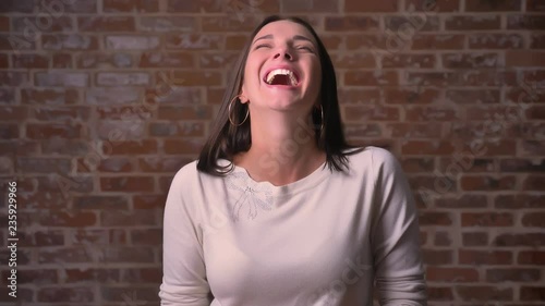 Woman watches to the camera and then starts laughing hard on a bricken background. photo