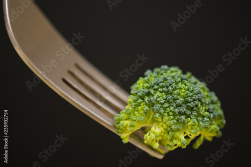 A green broccoli and a steel fork in a dark background