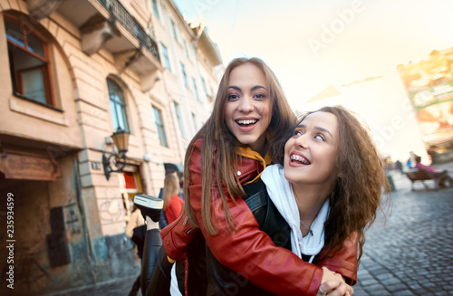 two young girls walking city laughing and having fun. joyful Women in colored leather biker jackets and hoodies walking on the street photo