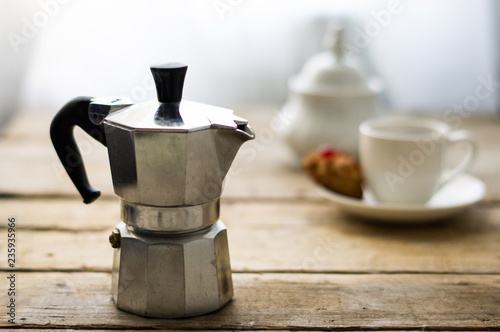 Traditional italian coffee maker with sweets and porcelain cup with sugar-bowl in the background