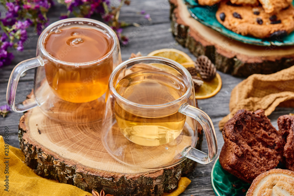 two glass cups of tea on a wooden saw, with cookies and dried flowers on the background. wooden background. autumn tea composition. close-up two glass cups of tea on a wooden saw, with cookies and dried flowers on the background. wooden background. autumn tea composition. close-up