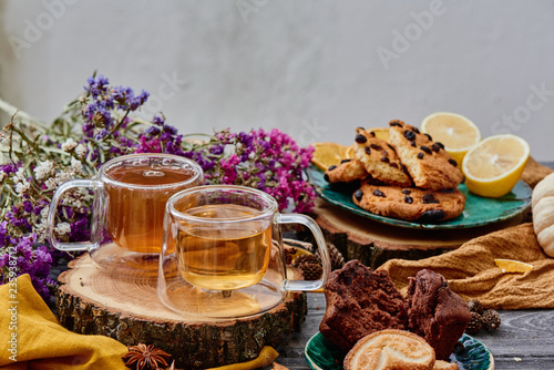 two glass cups of tea on a wooden saw, with cookies and dried flowers on the background. wooden background. autumn tea composition. close-up