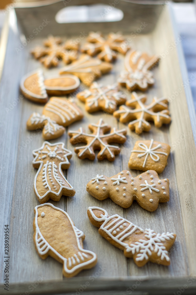 Fototapeta premium Painted traditional Christmas gingerbreads arranged on wooden tray in daylight, snowflakes and other Xmas symbols