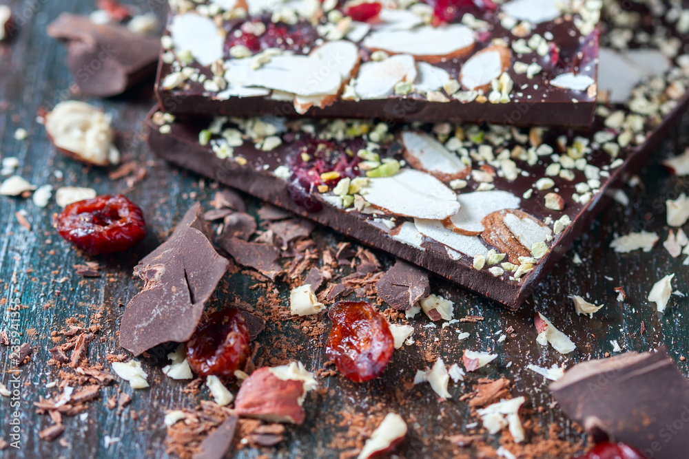 Homemade dark chocolate bar with dried berries and nuts on black background