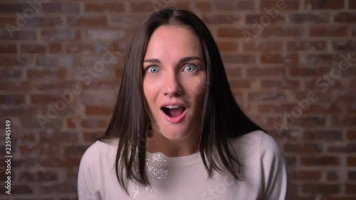 Woman watches into camera with strong positive shock on a bricken background