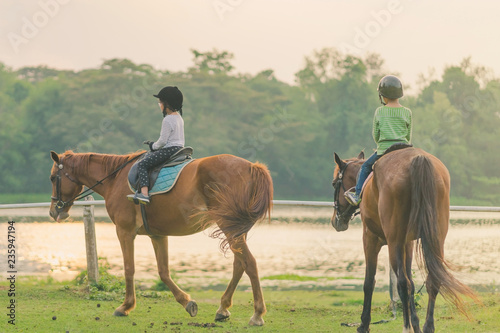 Kids learn to ride a horse near the river before sunset. © JinnaritT
