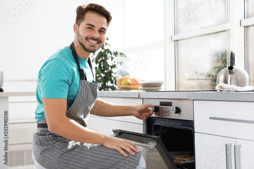 Young man baking cookies in oven at home