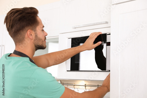 Young man using modern microwave oven at home