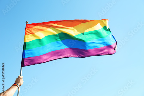 Gay man holding rainbow LGBT flag on blue sky background