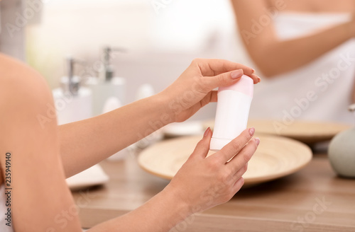 Young woman holding deodorant in bathroom, closeup
