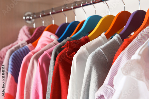 Stylish girl's clothes hanging in wardrobe, closeup