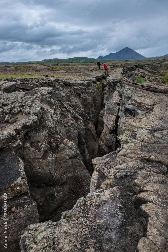 Dramatic view of deep volcanic crustal crack, hiking trail and hikers on Iceland, summer time