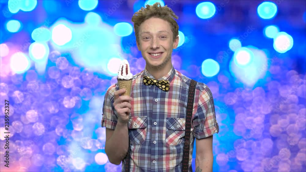 Happy teen guy holding an ice cream. Portrait of cute smiling teenage boy with ice cream cone on blue bokeh lights background.