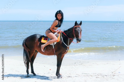 Sexy girl in black bikini riding horse at beach. A lot sun bath make her skin look very nice tan.
