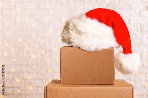 Obraz na plátně Blank brown freight box with Santa Claus hat on top, brick wall with Christmas lights on background