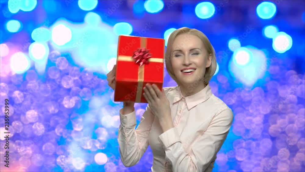 Surprised woman examines gift box. Happy satisfied girl with Christmas gift on blue bokeh background. Winter holiday present.