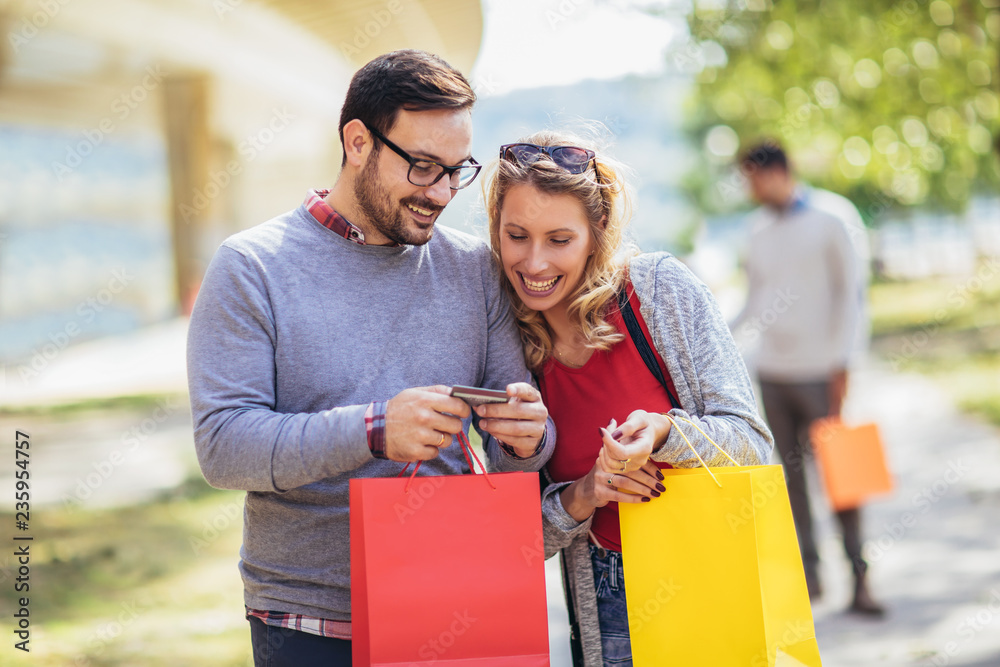 Portrait of happy couple with shopping bags after shopping in city smiling and holding credit card
