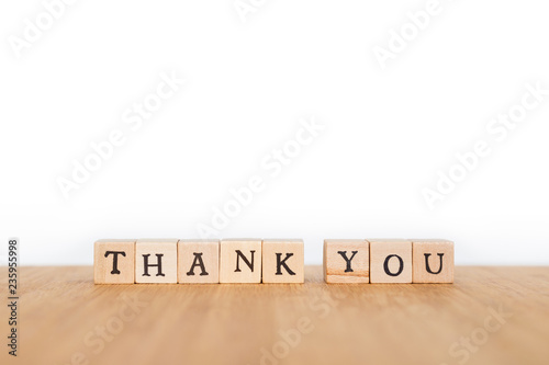 Focus on the phrase "Thank You" made of wooden block dice with letters on a wooden table. Shallow depth of field. Copy space.