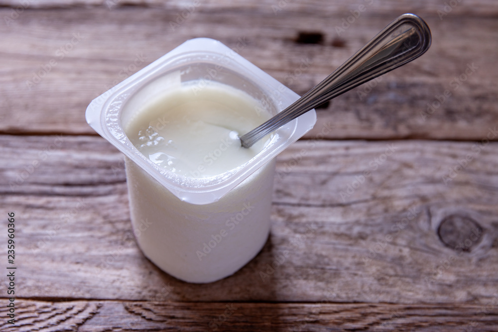 Natural yogurt in a plastic container on a rustic table Natural yogurt in a plastic container on a rustic table