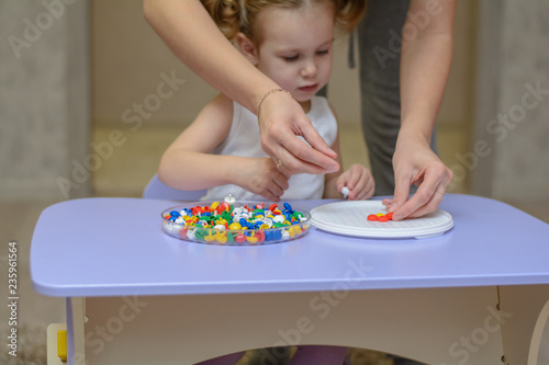 
A little funny baby girl is playing with colorful cubes. She builds different figures with her mom. The girl is sitting at her desk at home. Children's creativity. Educational games