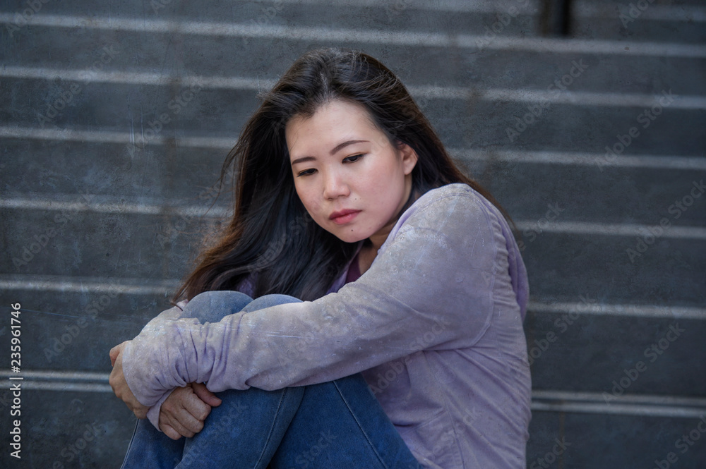 depressed Asian American student woman or bullied teenager sitting outdoors on street staircase overwhelmed and anxious feeling desperate suffering depression