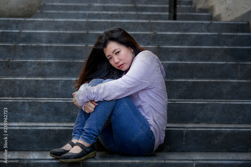 depressed Asian Chinese student woman or bullied teenager sitting outdoors on street staircase overwhelmed and anxious feeling desperate suffering depression