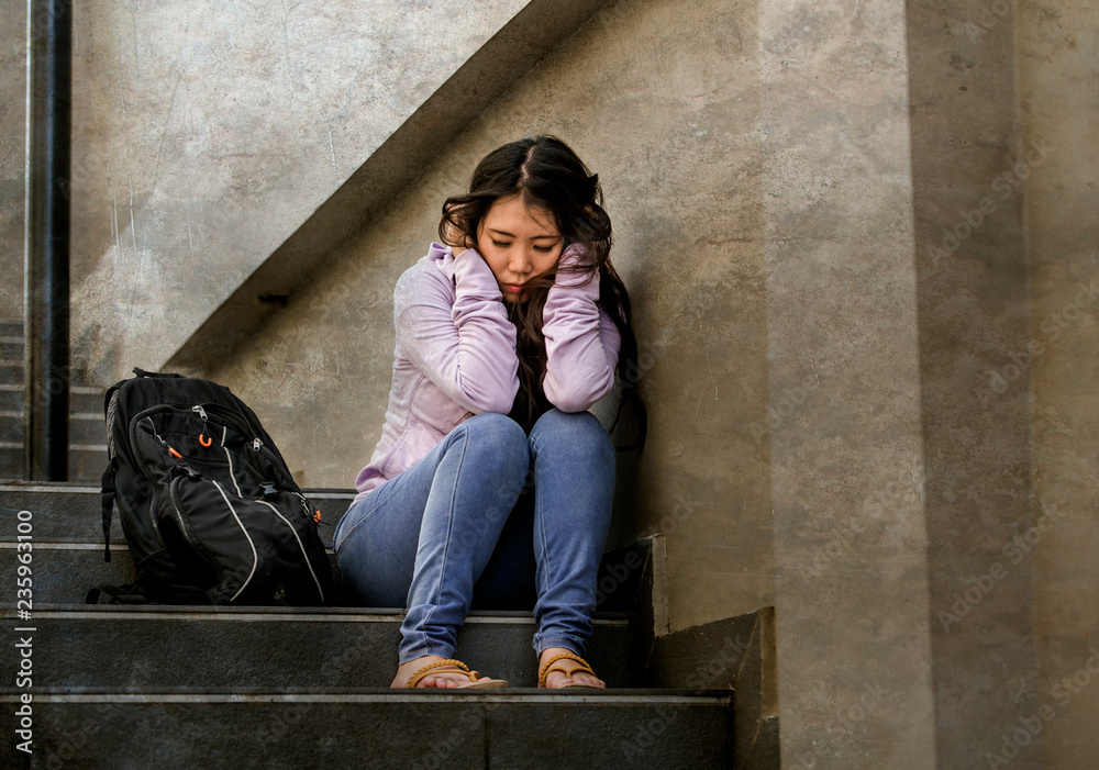 depressed Asian Japanese student woman or bullied teenager sitting outdoors on street staircase overwhelmed and anxious feeling desperate suffering depression