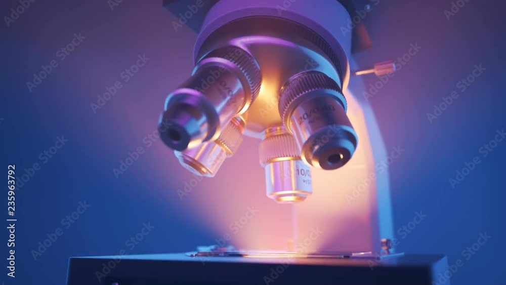 Modern microscope changing lenses in a laboratory. Light rays in the fog. 4KHD