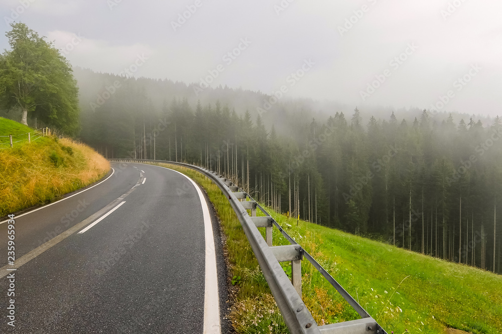 Beautiful mountain road in Austria. Misty forest and cloudy sky in background. Beautiful mountain road in Austria. Misty forest and cloudy sky in background.