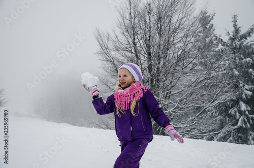 child with snowball in winter forest