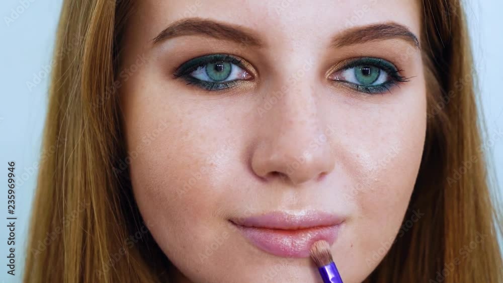 young woman putting lipstick with makeup brush closeup. people, cosmetics, lifestyle concept young woman putting lipstick with makeup brush closeup. people, cosmetics, lifestyle concept